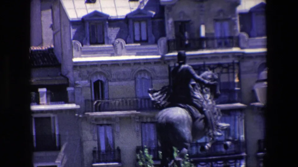 1967 Madrid travel footage frame with an equestrian monument, multi-story historic facades, balconies, and a central dark foreground obstruction.