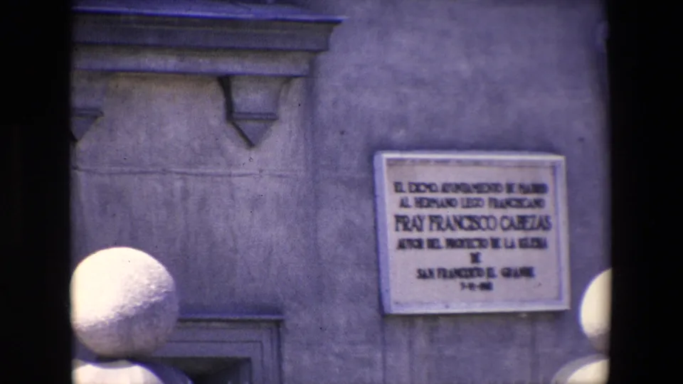 1967 Madrid frame showing a stone wall with a Spanish commemorative plaque below the partly visible equestrian statue and surrounding architectural details.