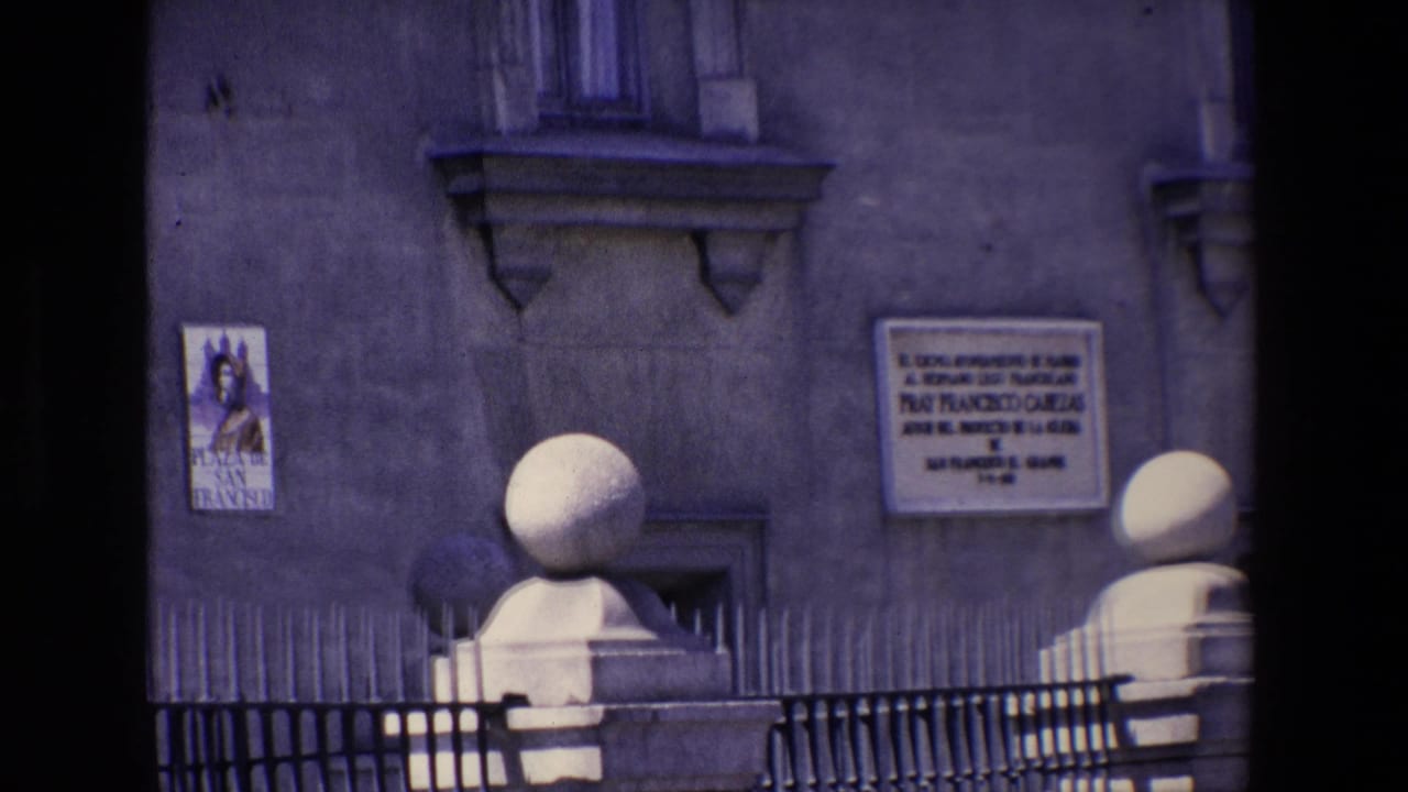 Building wall with Spanish plaques, religious-style poster, iron fence, and stone posts.