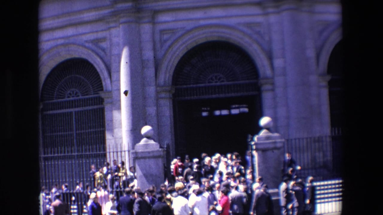 1967 Madrid home-movie frame showing people clustered near the steps and iron gates of a large arched stone building entrance.