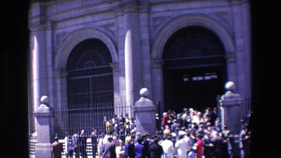 1967 Madrid frame with a crowd gathered beside iron fencing and an arched doorway on a large public-looking stone facade.