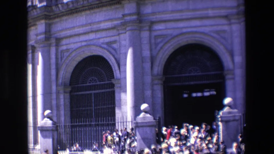 1967 Madrid frame showing people gathered tightly near an iron fence and dark arched doorway on a stone building exterior.