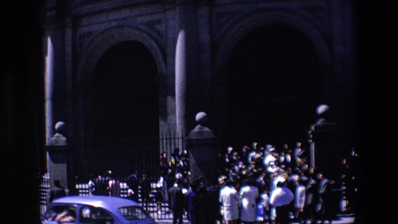 Crowd gathered near a large arched stone entrance with a car in the foreground.