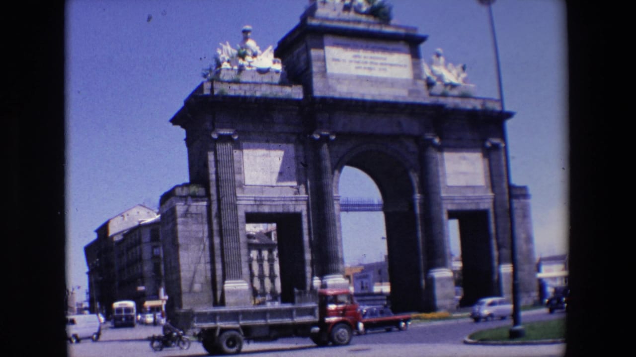 Large stone monument beside a road with cars, a red truck, and small motorcycles passing.
