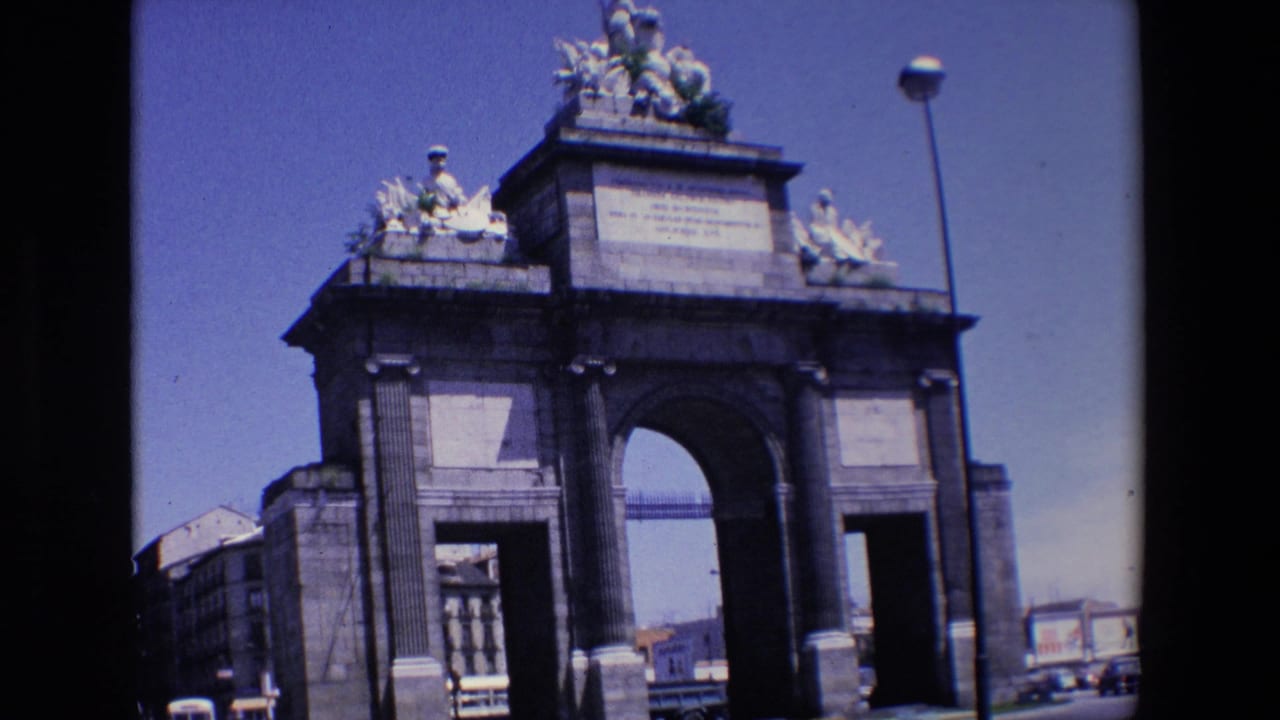 Monumental arched stone gateway with rooftop sculptures and traffic in the distance.