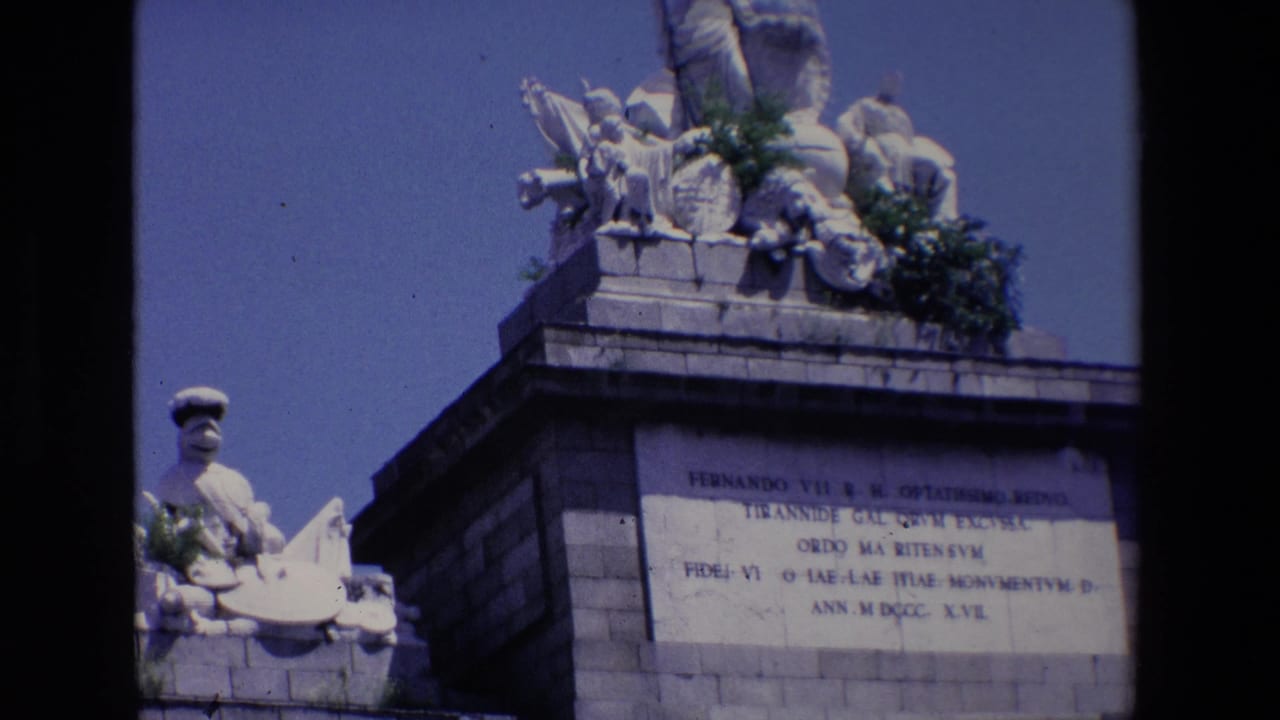 Stone monument with inscription panel, sculpture above, and dark film border at left.