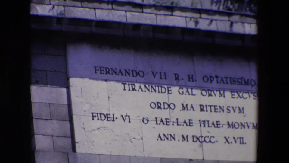 1967 Madrid 8mm frame showing a large carved inscription panel on a stone monument, with "Fernando VII" legible and dark gate-edge shadow crossing the frame.