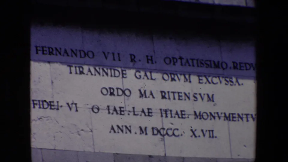 1967 Madrid 8mm frame showing the lower contact-sheet view of the Fernando VII stone inscription, with block seams and partial Latin lettering visible.