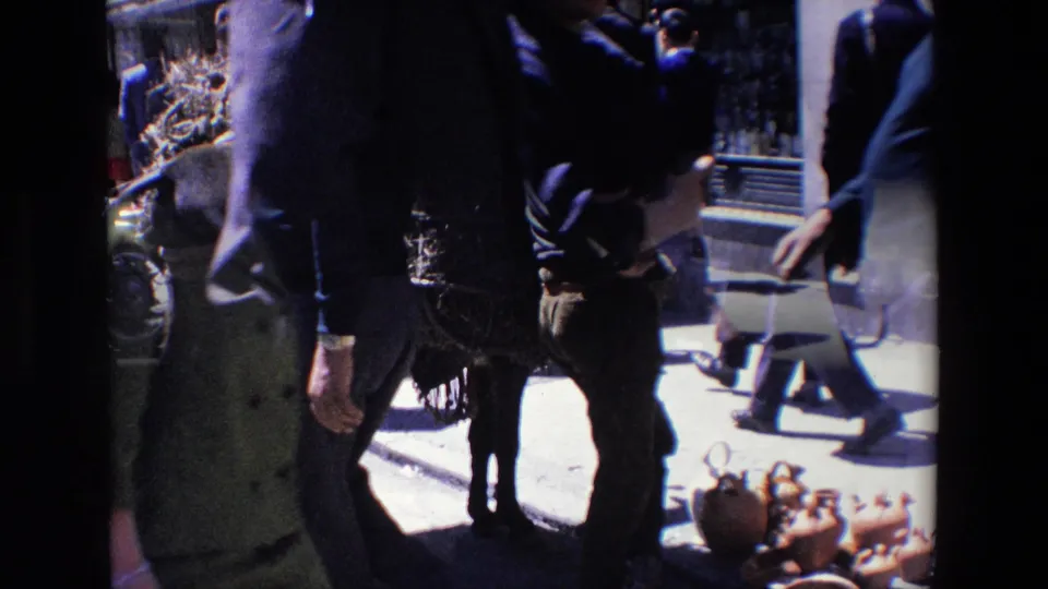 1967 Madrid street footage frame with pedestrians crossing in front of a donkey and clay pottery display, partially obscured by the handheld camera framing.