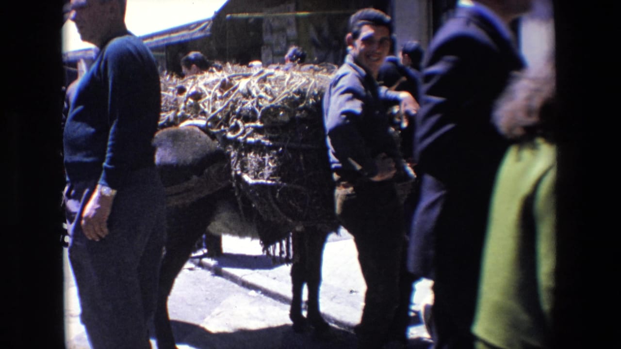 1967 Madrid home-movie frame showing a man near a heavily loaded animal or cart, with pedestrians close to the camera and strong daylight on the street.