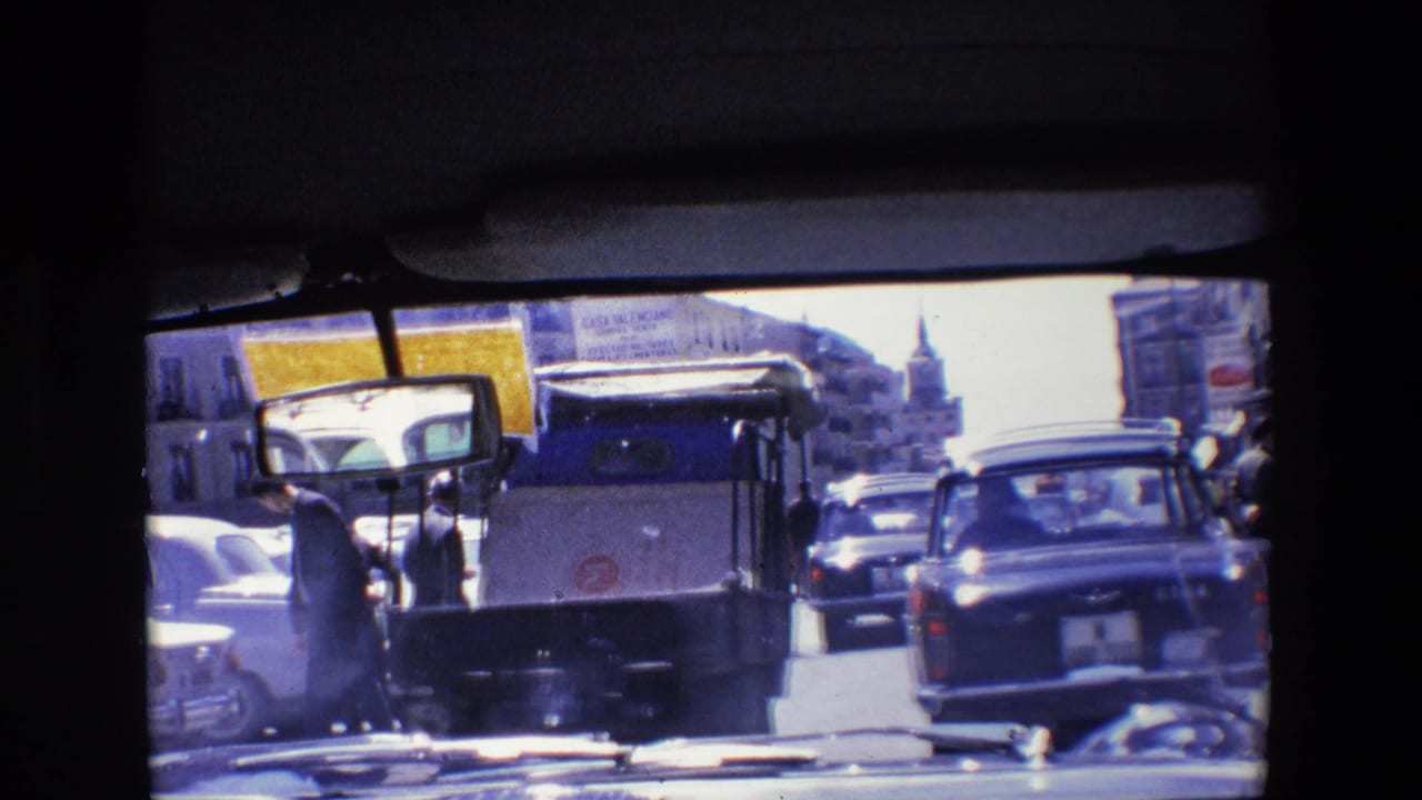 Street traffic with a small utility vehicle and cars seen through a dark window frame.