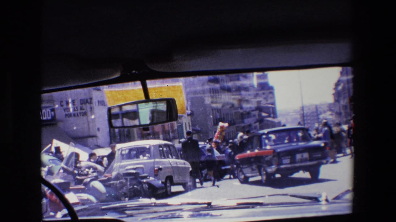 View through a vehicle windshield toward cars and pedestrians on a crowded city street.