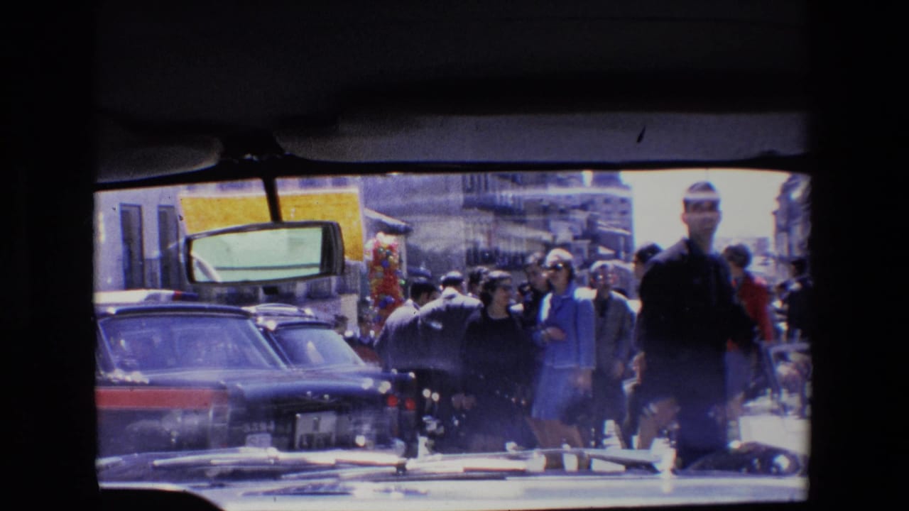 Pedestrians and cars on a busy street seen through dark window framing.