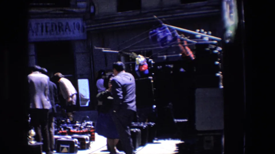 Madrid 1967 street view with pedestrians gathered around outdoor merchandise racks in front of a dark shop entrance and partial Spanish signage.