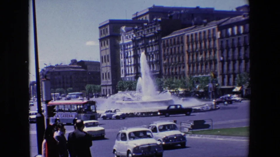 1967 Madrid street scene showing a bus and several cars moving past a spouting fountain, with pedestrians partly visible at the lower left.