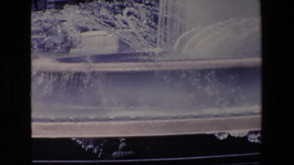 1967 Madrid frame focused on the large public fountain's spray and basin, with the roadway edge and dark contact-sheet border visible in the foreground.