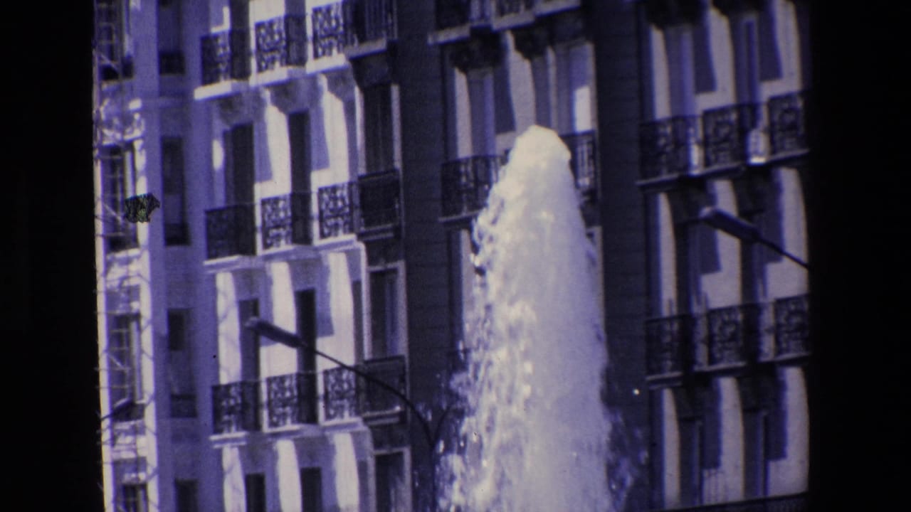 The fountain continues gushing upward beside a multi-story facade with railings, windows, and a street light, matching the Madrid 1967 clip metadata.
