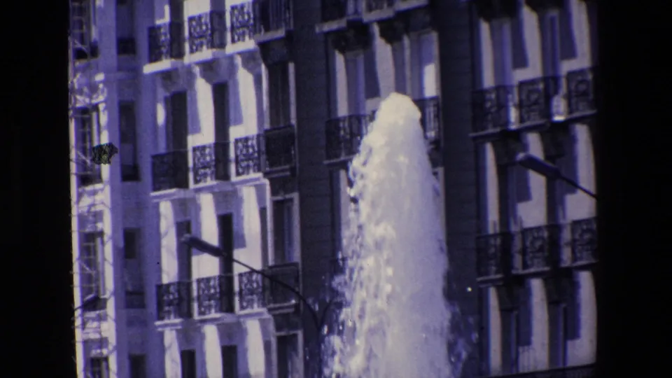 The fountain continues gushing upward beside a multi-story facade with railings, windows, and a street light, matching the Madrid 1967 clip metadata.