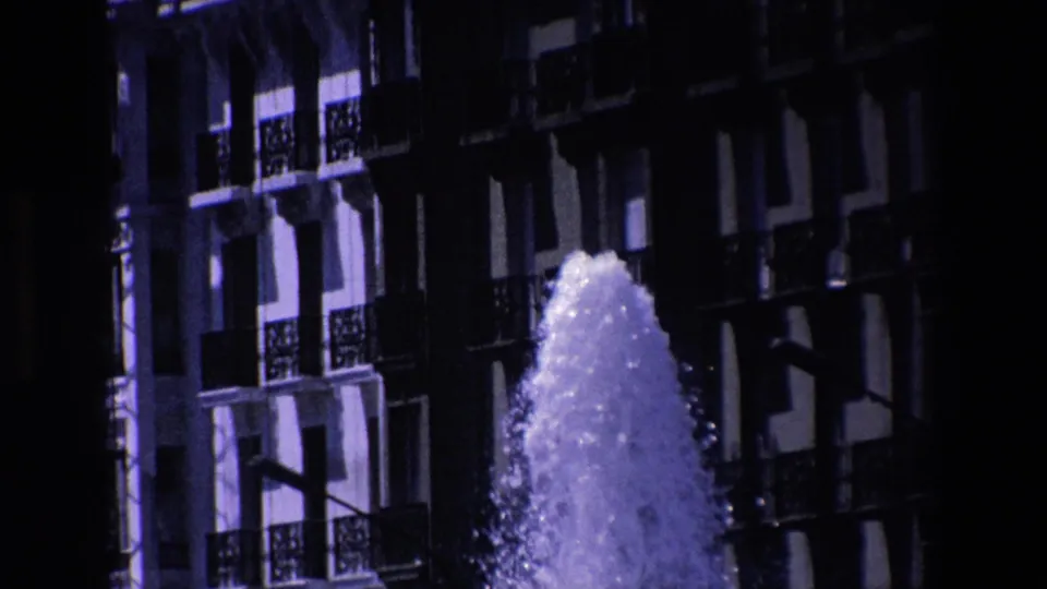 The final frame shows the fountain plume against a darker section of the Madrid building facade, with balcony rails, windows, and a street light visible through high contrast.