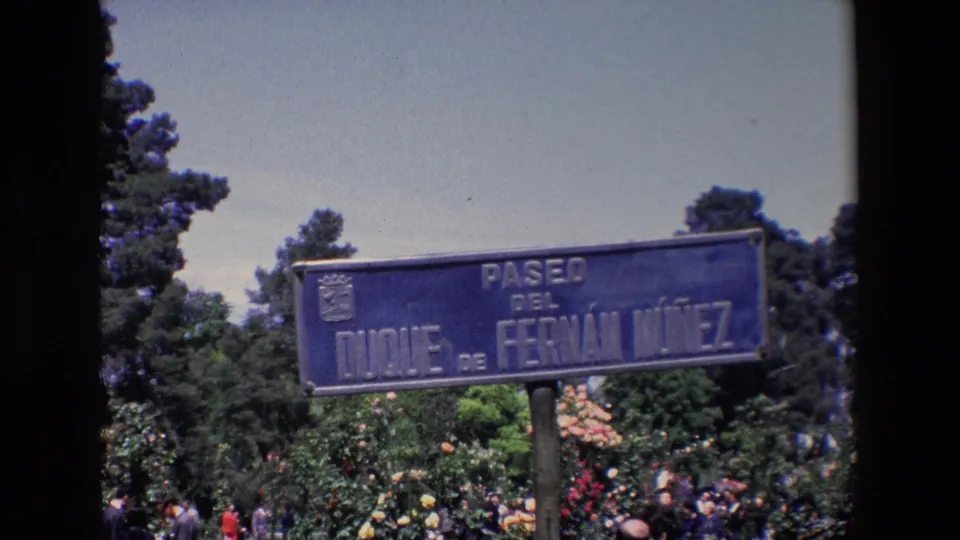 1967 Madrid frame with the Paseo del Duque de Fernan Nunez sign centered above trees and partially visible formal guests.