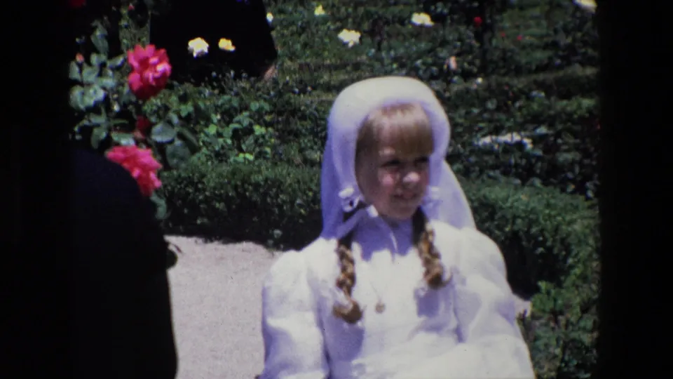 The 1967 Madrid footage shows a young girl in a white veil and formal white clothing facing the home-movie camera in a rose garden.