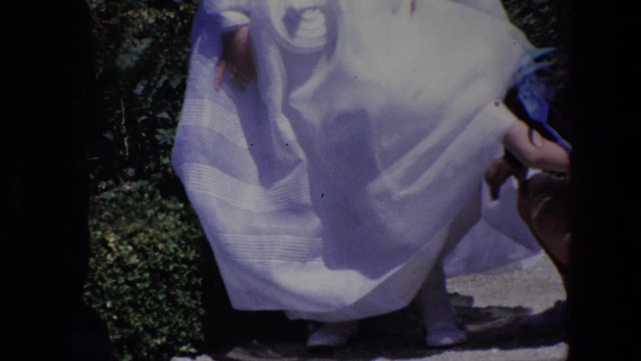 Madrid 1967 8mm frame showing children in white formal dress in a garden, with one child partly obscured by a foreground skirt and dark film borders.