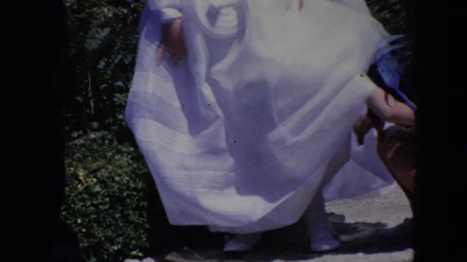 Madrid 1967 8mm frame showing children in white formal dress in a garden, with one child partly obscured by a foreground skirt and dark film borders.