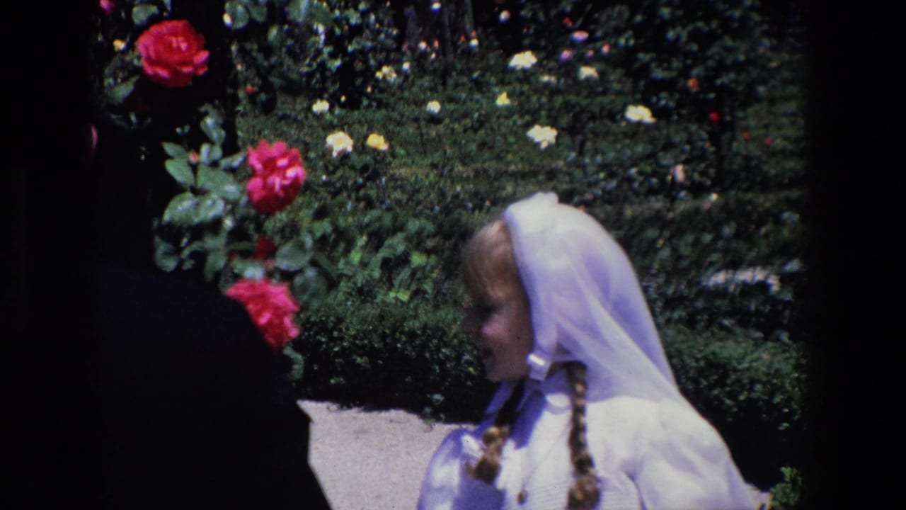 Girl in a white veil and dress standing near rose bushes outdoors.