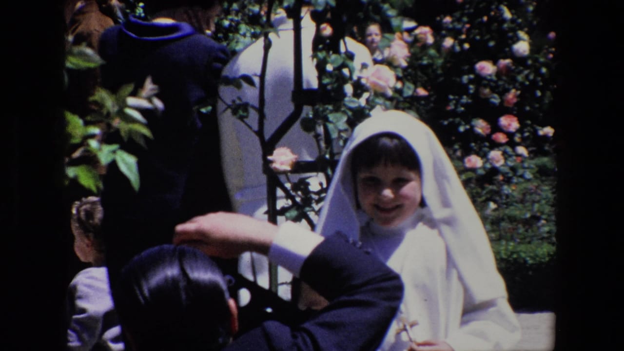 Smiling girl in a white veil facing an adult with a camera in a rose garden.