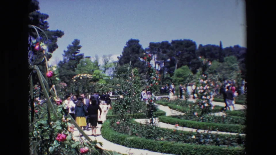 1967 Madrid garden view with groups of visitors walking along winding paths among rose bushes, hedges, and trees.