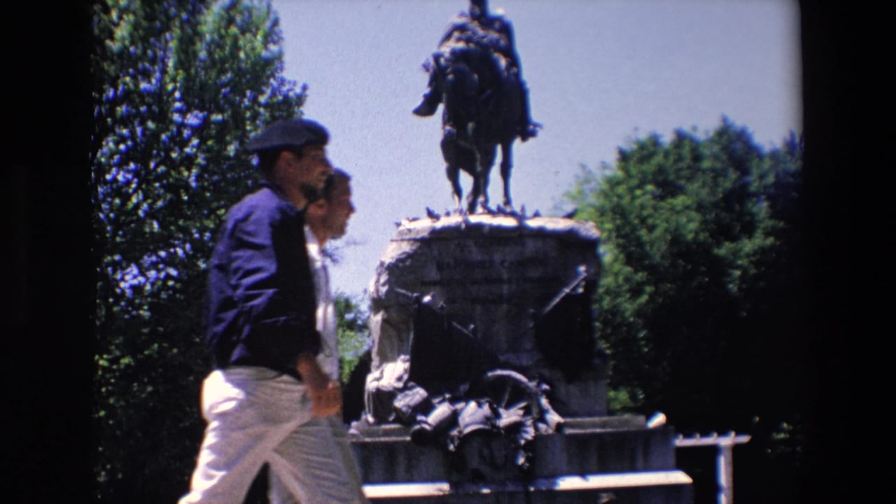 In Madrid, Spain, a visitor-shot 1967 8mm frame shows two pedestrians walking past the stone base of the General Arsenio Martinez Campos equestrian monument.