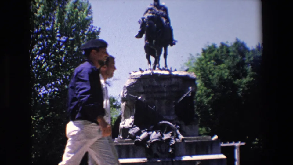 In Madrid, Spain, a visitor-shot 1967 8mm frame shows two pedestrians walking past the stone base of the General Arsenio Martinez Campos equestrian monument.