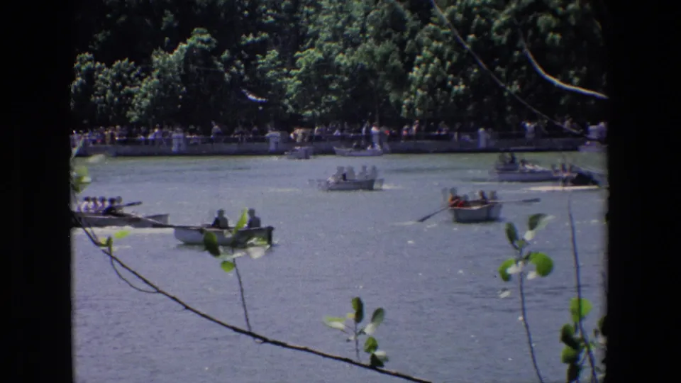 1967 Madrid frame showing people in small boats near a tree-lined bank, with foreground branches crossing the lake view.