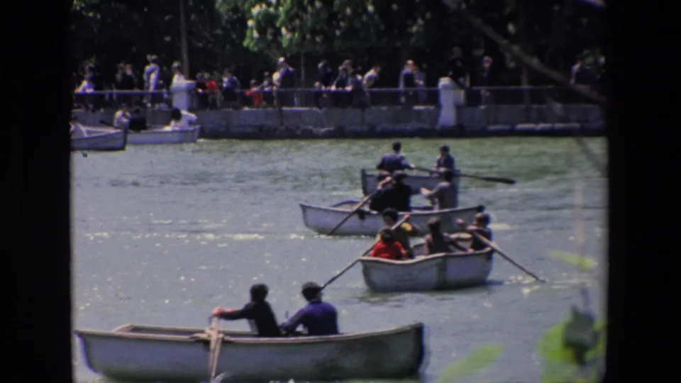 1967 Madrid frame showing clustered rowboats with seated passengers, oars extending across the water, and a busy waterside promenade in the background.