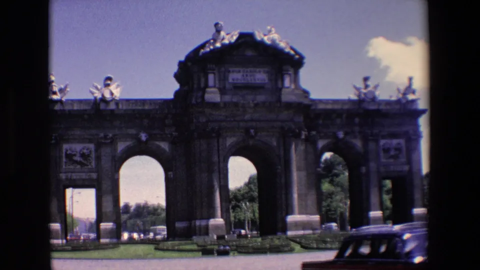 1967 Madrid view of the Puerta de Alcala with arched stone openings, sculptural details, lawn edges, and classic cars on the surrounding road.