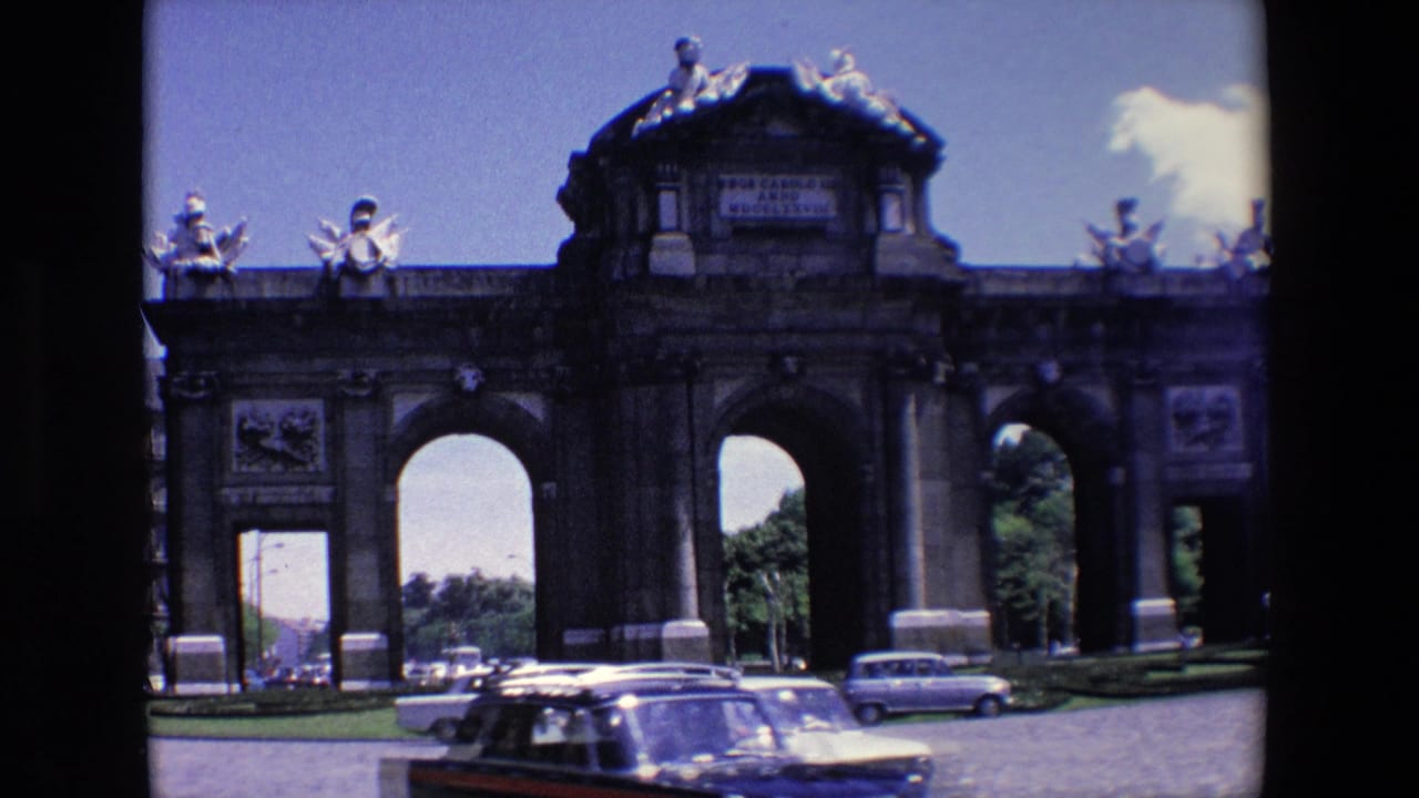 Historic stone gateway with statues above and several cars on the road in front.