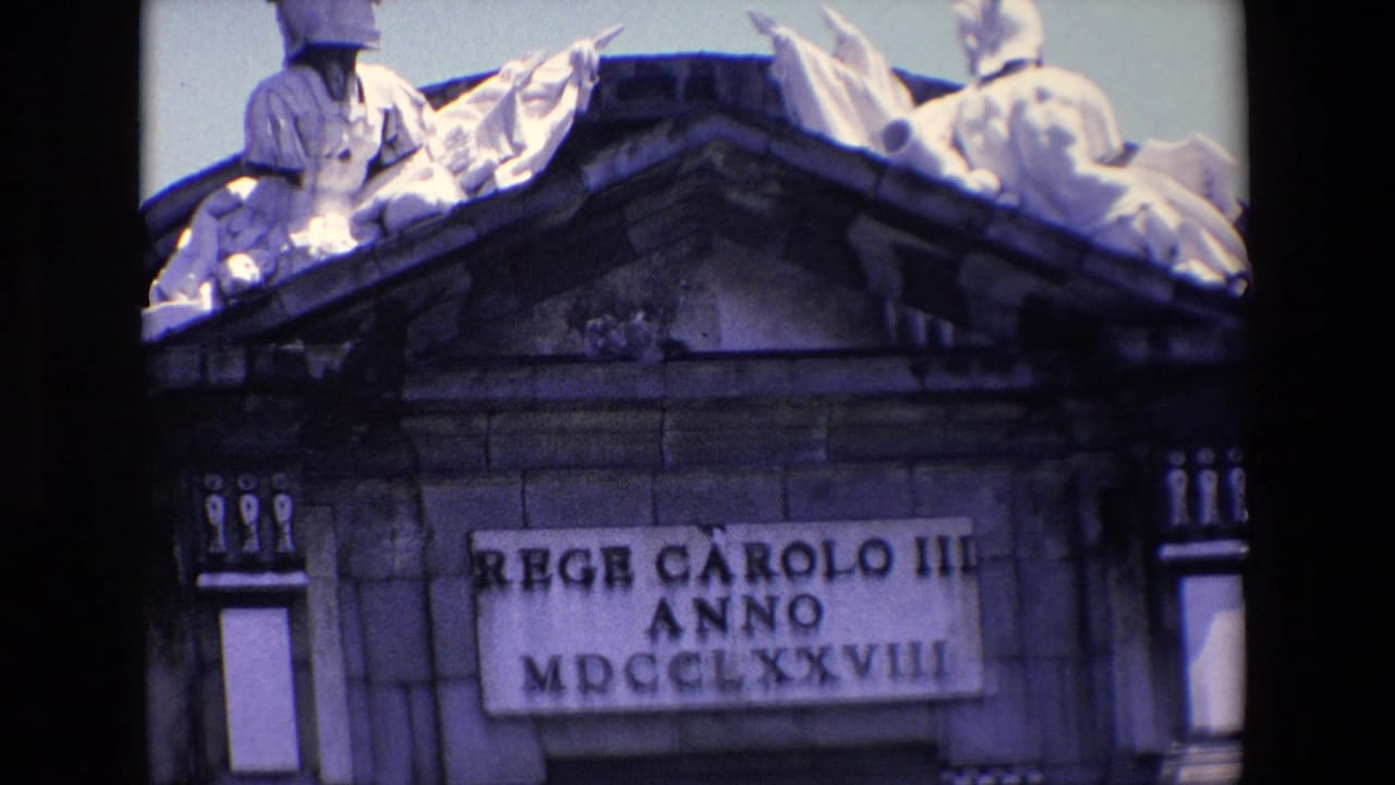 Wider view of a stone pediment with sculpted figures above an inscribed plaque.