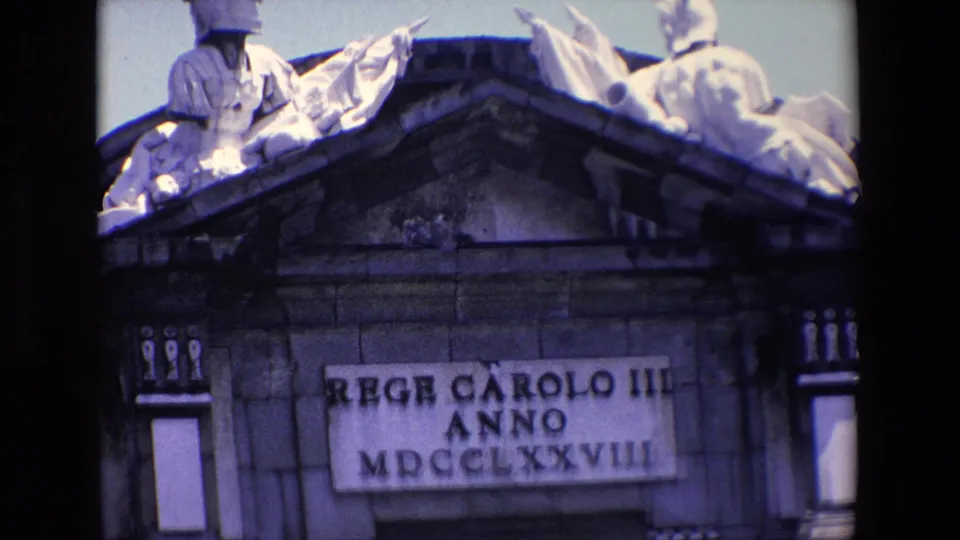 Madrid 1967 home-movie frame showing a weathered stone architectural detail with sculpted figures above a rectangular plaque bearing Roman-style lettering and numerals.