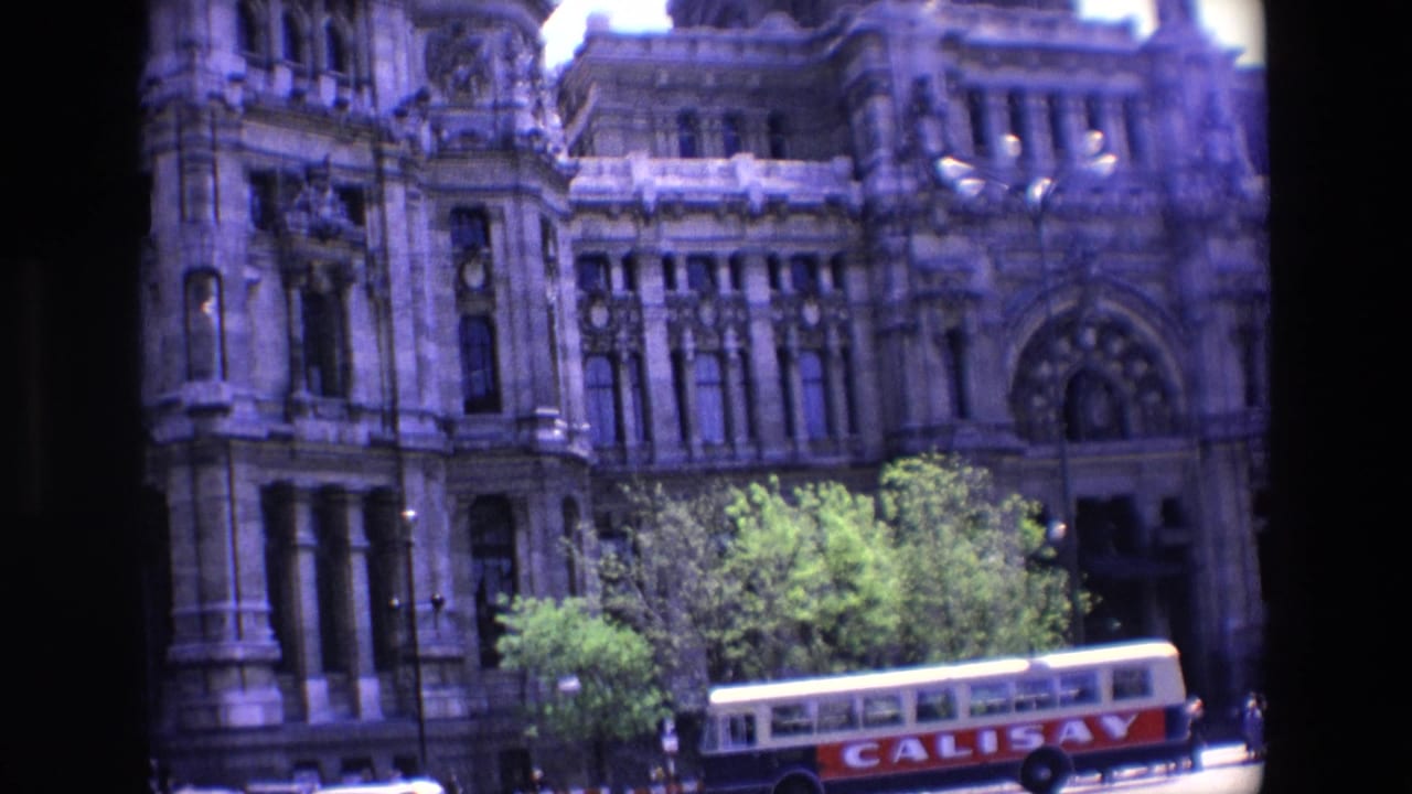 Ornate building facade with trees and a bus along the street below.