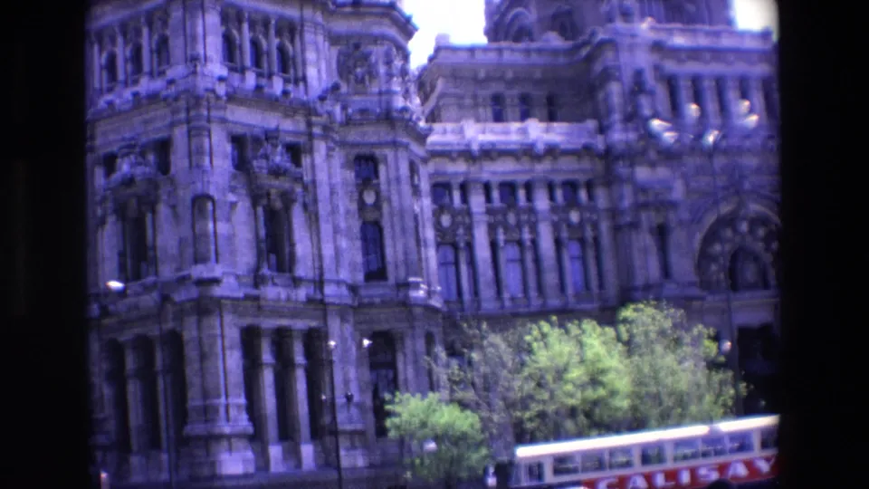 1967 Madrid 8mm frame showing a closer, soft-focus view of an ornate stone building corner, street trees, and a bus partly cut off at the bottom.