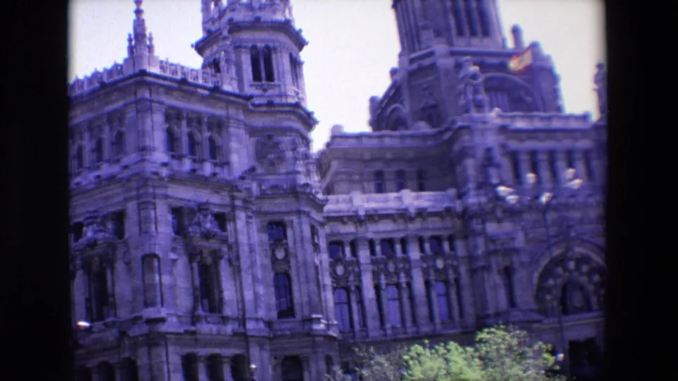 1967 Madrid 8mm frame showing a grand ornate stone facade with a tower, arched windows, roofline detail, and green trees below.