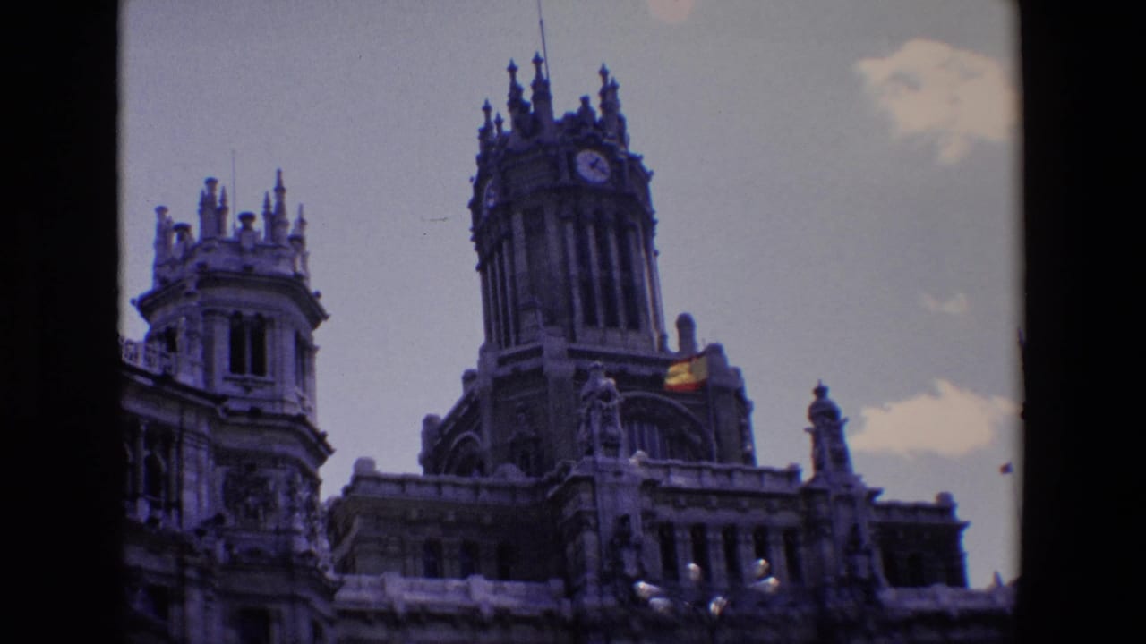 Clock tower and adjoining spired facade with a small Spanish flag visible near the roofline.