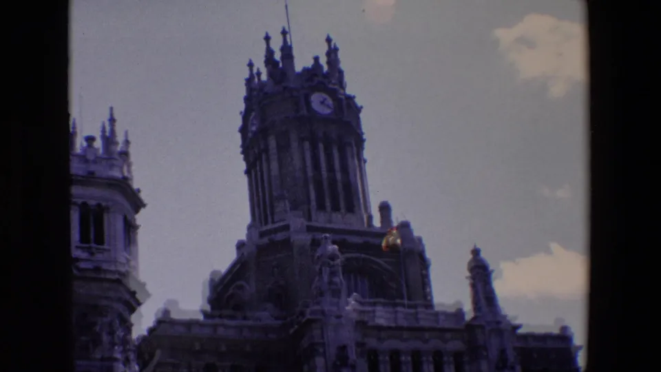 1967 Madrid home-movie still showing a closer visitor view of the clock tower and sculpted upper facade with a Spanish flag near the roofline.