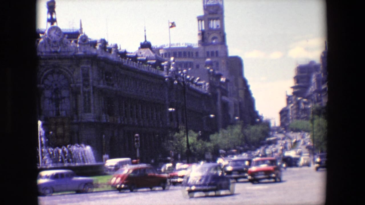Busy Madrid avenue with cars passing a fountain and ornate building with a clock tower.