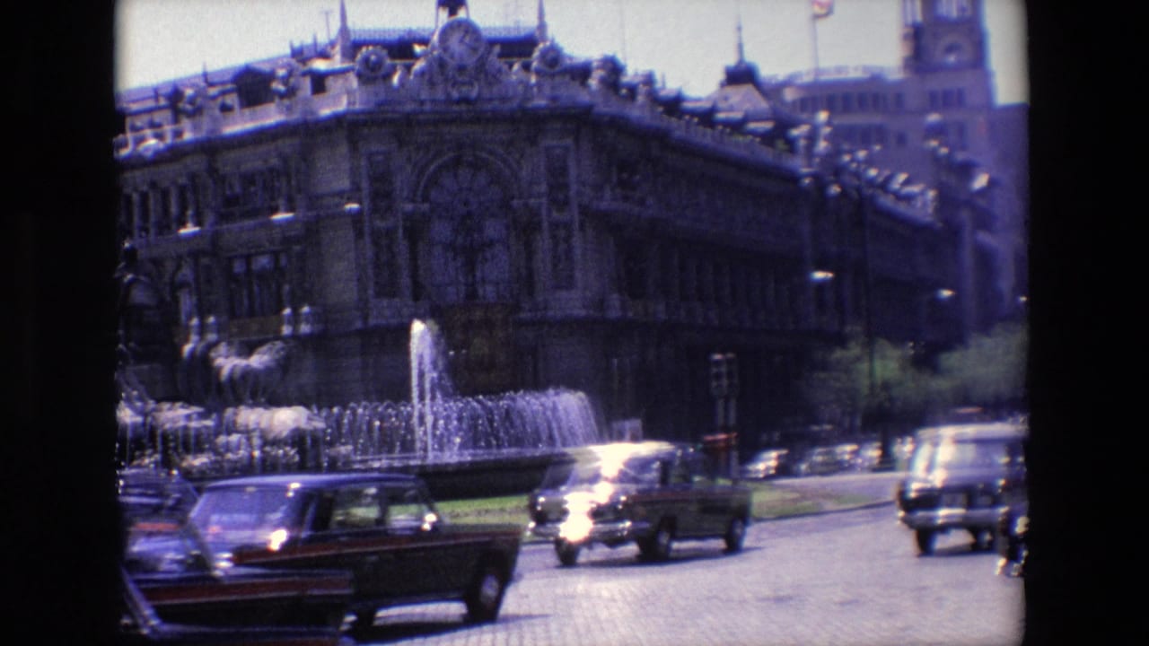 Cars pass a fountain in front of a large ornate building.