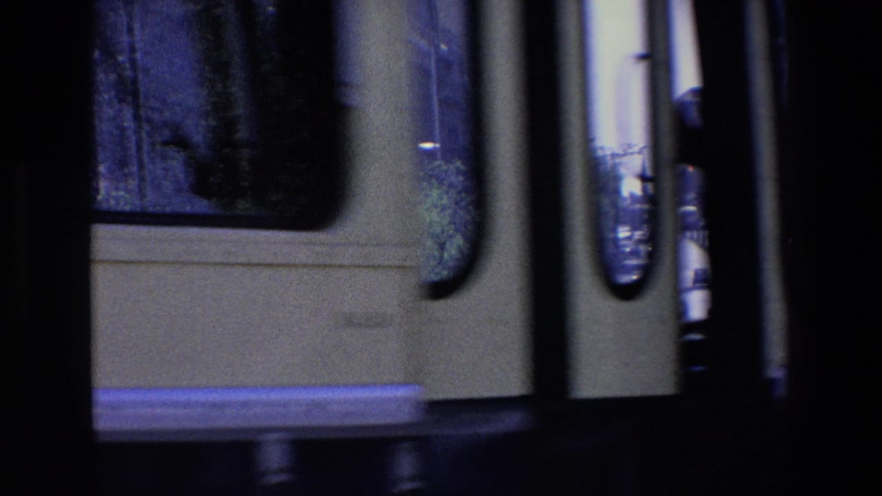 Partial vehicle side seen close to camera with a city street visible beyond dark film borders.