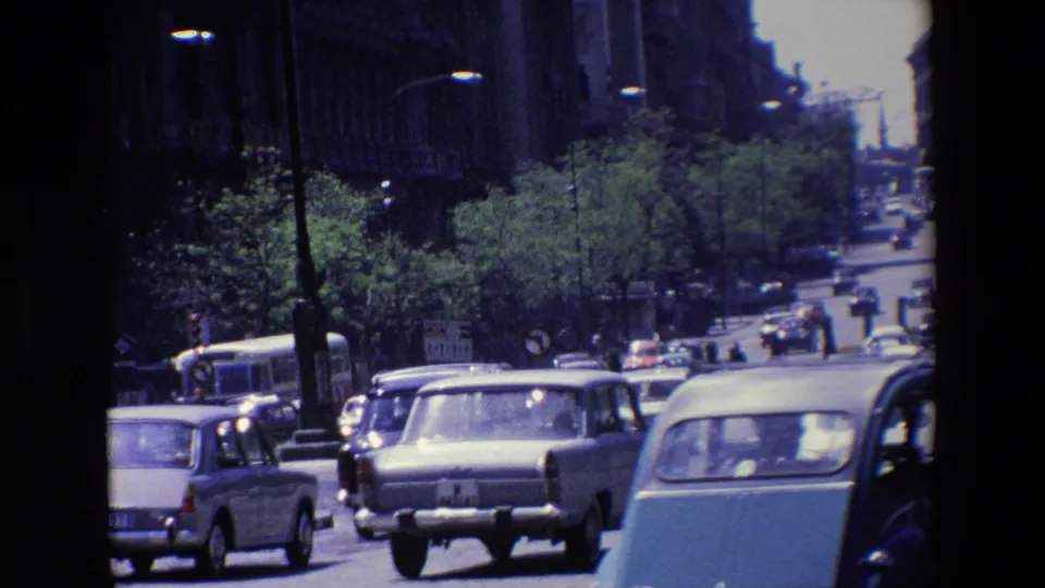 1967 Madrid home-movie view of dense daylight traffic, including compact cars, a larger sedan, and a bus along a tree-lined urban road.