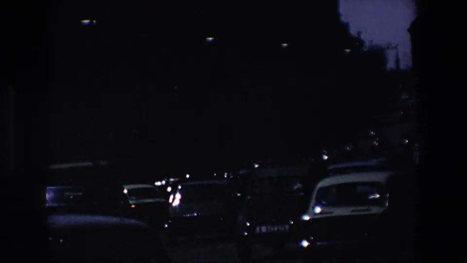 Underexposed 8mm frame from the same Madrid travel sequence showing dark roadway silhouettes, vehicle lights, and heavy shadow at the end of the clip.