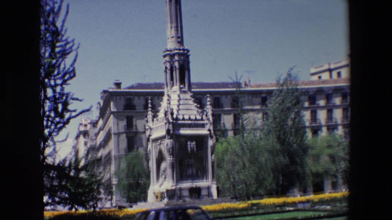 Stone monument and column seen across grass and yellow flower beds.