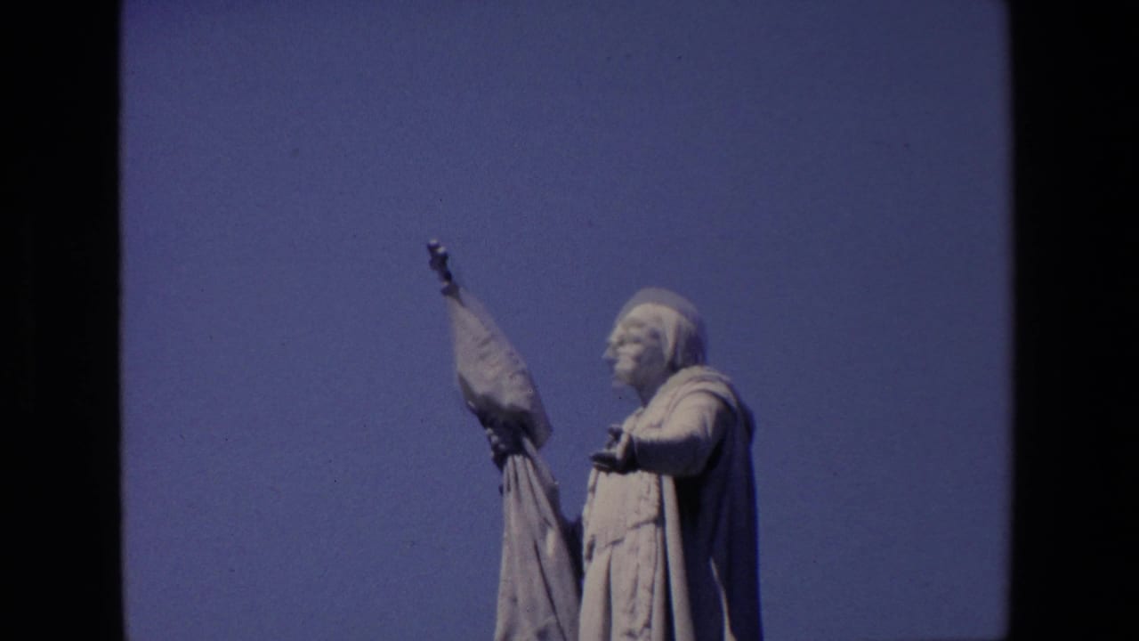 Stone statue holding a flag against a clear blue sky.